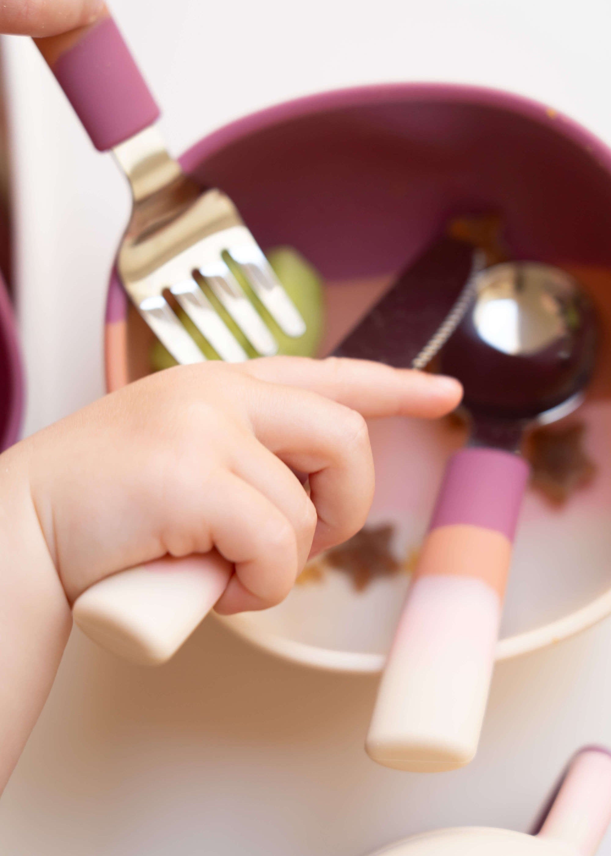 Toddler hand holding Grech & Co Blossom Ombre pink fork over matching silicone bowl with spoon inside — baby led weaning cutlery set at Milimilu