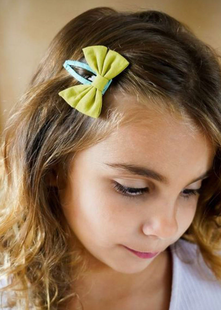 Girl wearing olive green organic cotton bow hair clip with blue snap clip in wavy hair — Grech & Co kids hair accessories at Milimilu