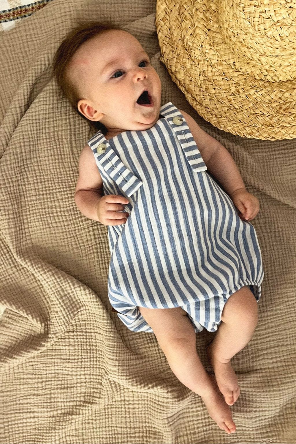Baby wearing blue striped organic romper; close up showing adjustable straps and snap button details