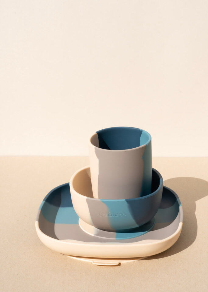 Grech & Co blue silicone toddler mealtime set with cup, bowl and plate in teal and stone tones on warm beige background — sustainable kids tableware at Milimilu