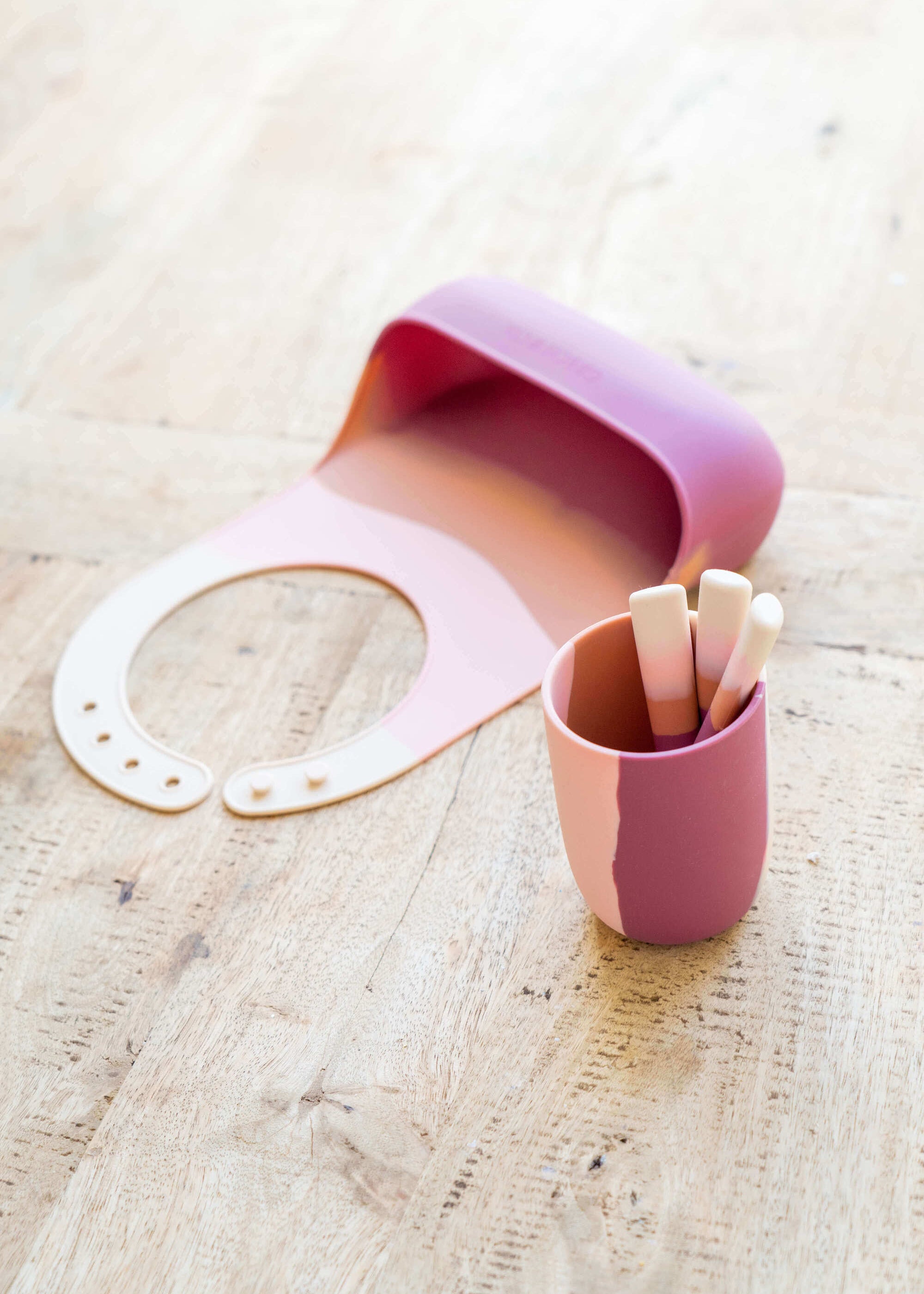 Grech & Co pink silicone toddler cup with cutlery and silicone bib in blush and terracotta tones on wooden surface — eco-friendly kids mealtime set at Milimilu