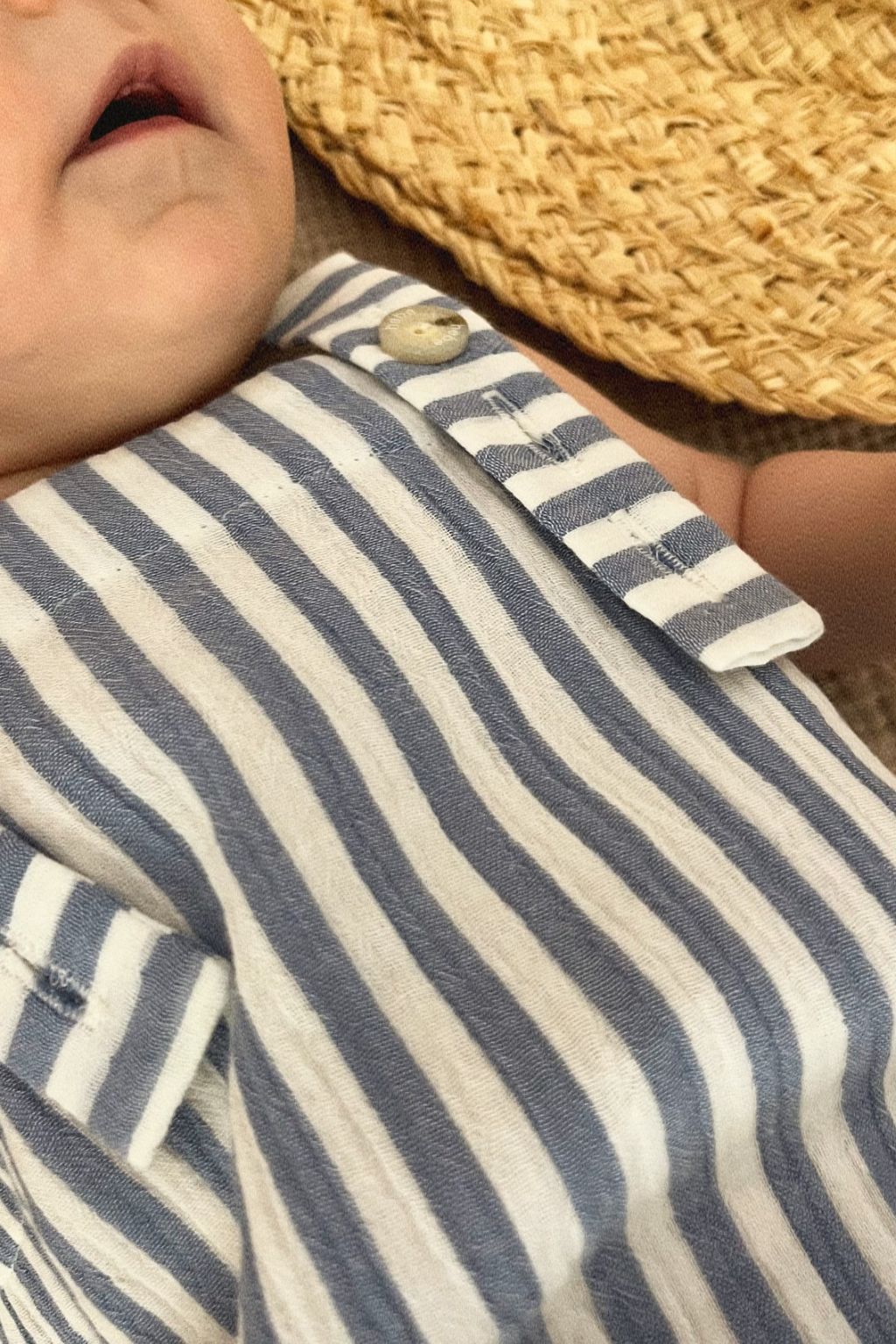 Baby wearing blue striped organic romper; close up showing adjustable straps and snap button details