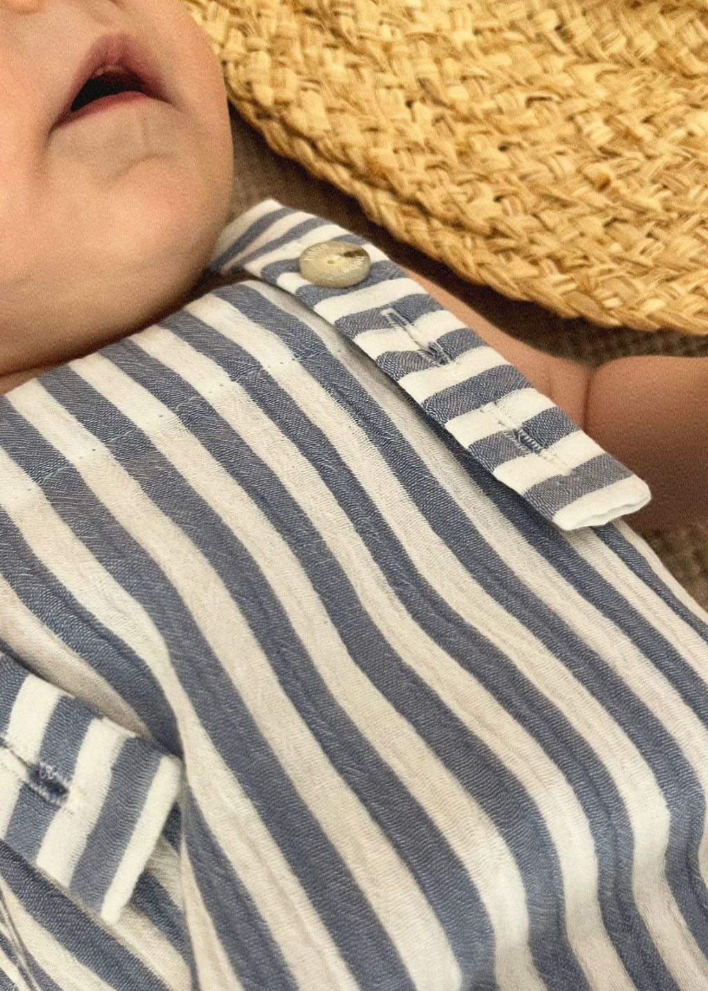 Baby wearing blue striped organic romper; close up showing adjustable straps and snap button details