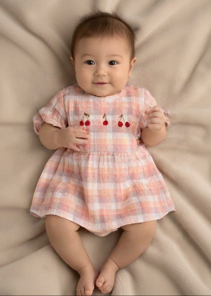 Baby girl wearing pink cherry embroidered organic cotton romper with puffed sleeves and ruffled skirt