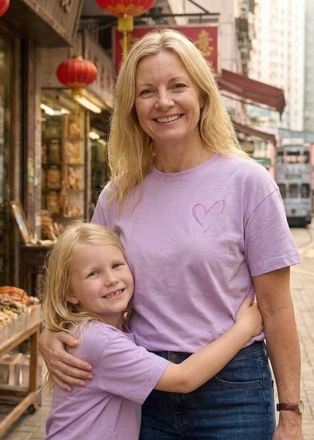 Woman and child in matching purple shirts standing on a street with shops and a tram in the background.