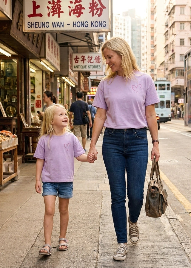Woman and child walking hand-in-hand on a street in Hong Kong with traditional shops and a double-decker bus in the background.