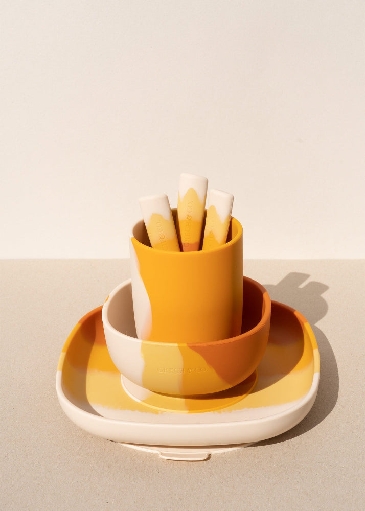 Grech & Co Sienna Ombre silicone suction plate stacked with bowl and cup holding cutlery in amber and cream tones on warm beige background — eco-friendly toddler mealtime set at Milimilu