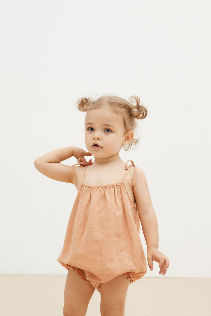 A light peach organic cotton baby girl summer romper is the most adorable outfit this summer. The organic cotton baby romper is breathable and made with lightweight extra soft organic cotton. Have adjustable straps and elasticated legs to fit your baby girl longer.  It is made by The New Society in Portugal. 
